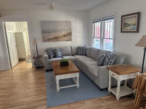 A living room with a sofa, coffee table, and side tables, a painting on the wall, and a door leading to another room.