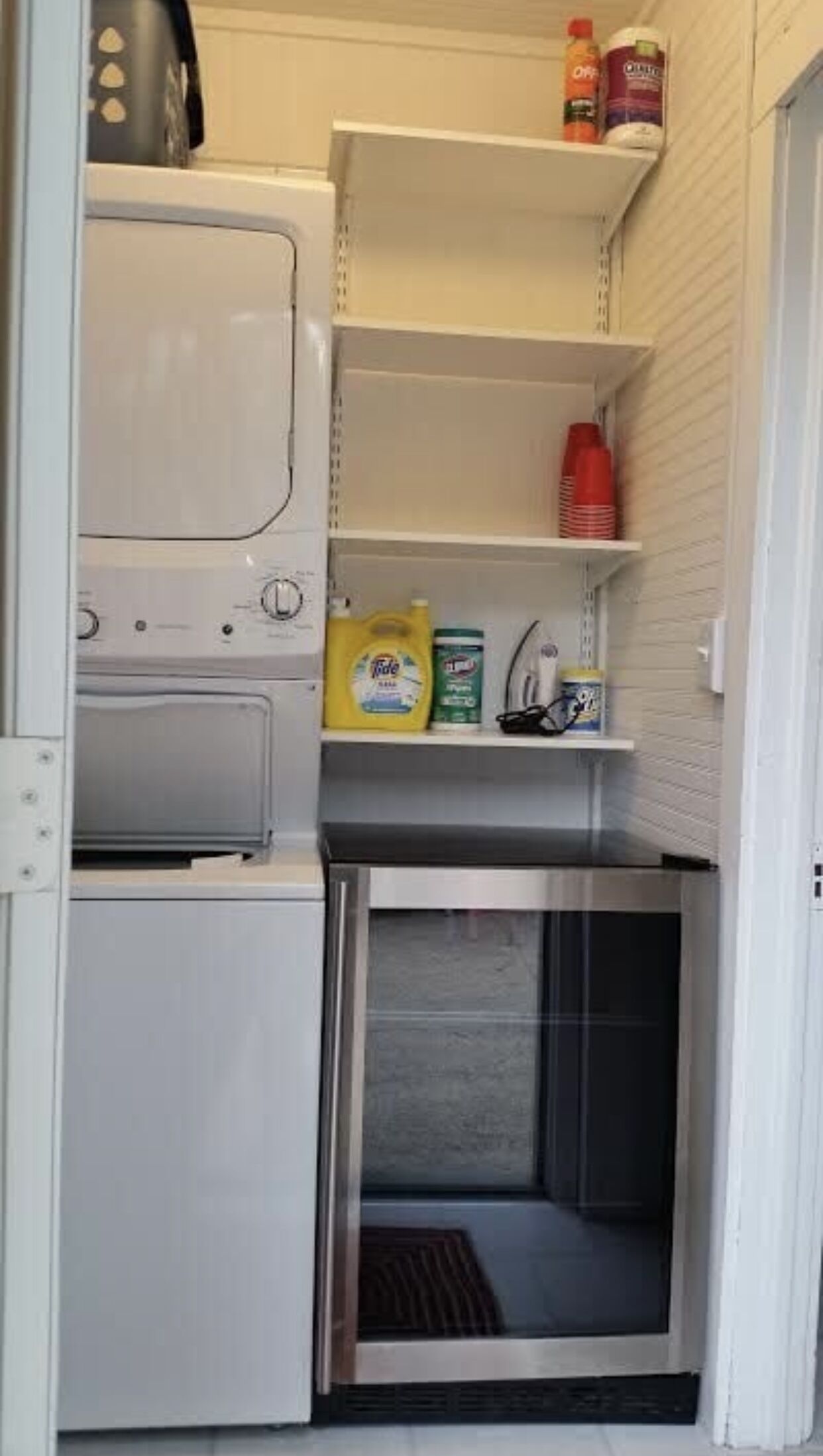 A compact laundry room with a washing machine, a dryer, and shelves containing cleaning supplies.