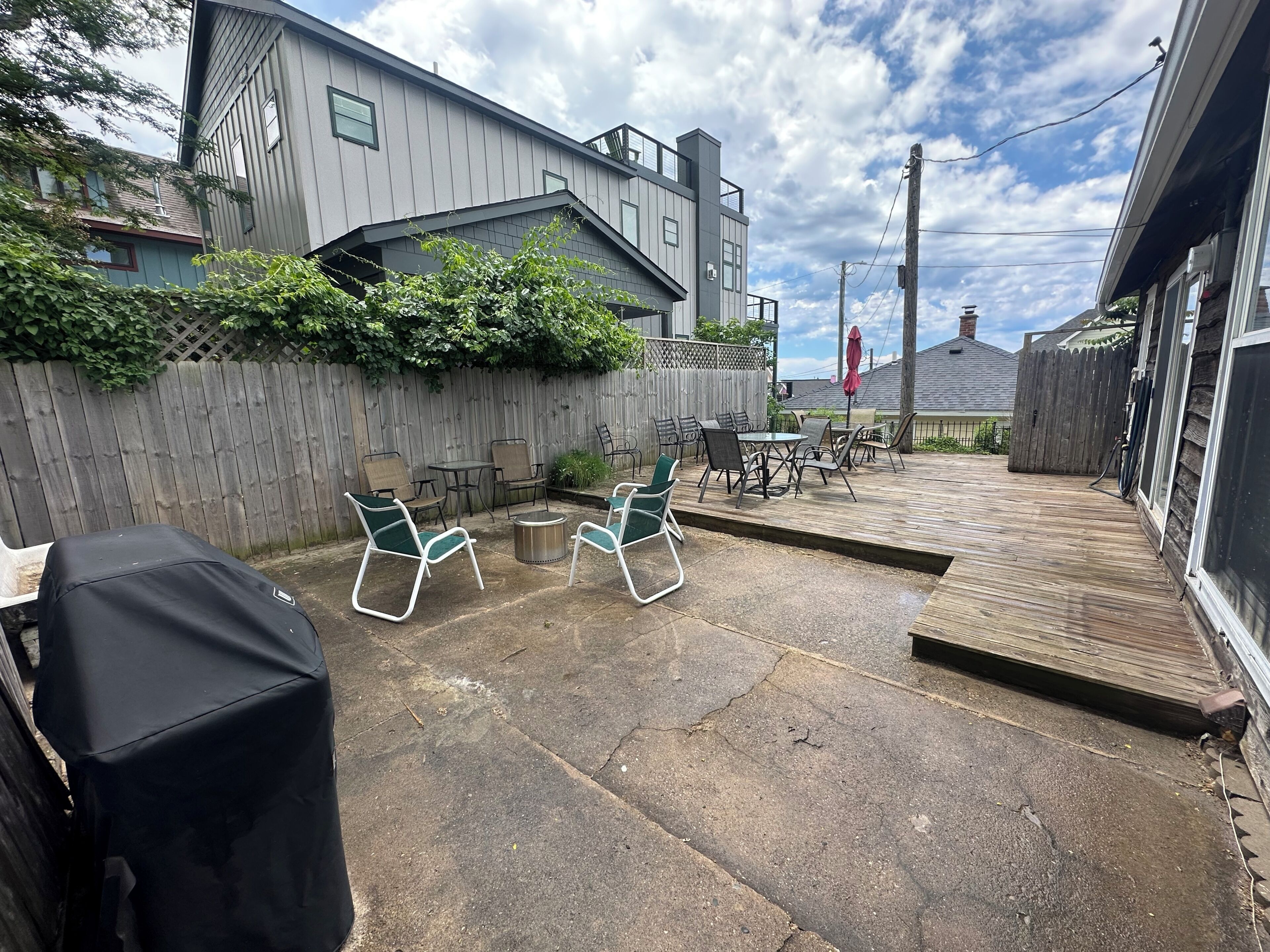 A backyard patio with outdoor furniture, a covered grill, and a wooden deck.