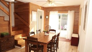 A wooden interior with a dining table, chairs, a ceiling fan, and a staircase.