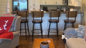 A modern living room with a sofa, a coffee table, and a patterned rug. There are three wooden chairs and a kitchen area with white cabinets and a refrigerator. - Lake side condo nearThe University of Alabama (Northport)