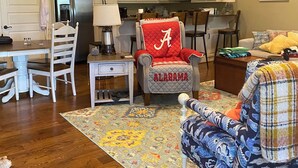 A spacious living room with a large wooden floor, a dining area with white chairs, a kitchen with white cabinets, and a ceiling fan. - Lake side condo nearThe University of Alabama (Northport)