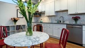 A modern kitchen with white cabinets, a marble table, and red chairs. - lower west side style & quality 1BR (Santa Cruz)
