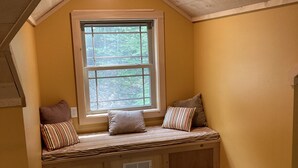 A cozy attic bedroom with a sloped ceiling, a large window, and a built-in bench with pillows.