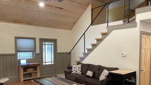 A spacious living area with a wooden ceiling, a staircase, a sofa with patterned cushions, a coffee table, and a small wooden side table.