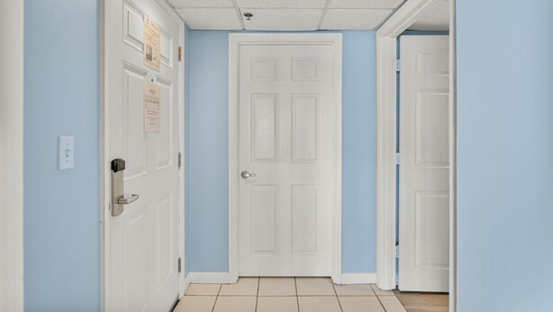 A hallway with light blue walls, white doors, and a tiled floor. - Long Beach 2-301 - 2322067 (Panama City Beach)