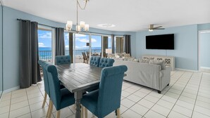 A spacious living room with a dining area, a large flat-screen TV, and a balcony with a view of the ocean. - Long Beach 2-301 - 2322067 (Panama City Beach)