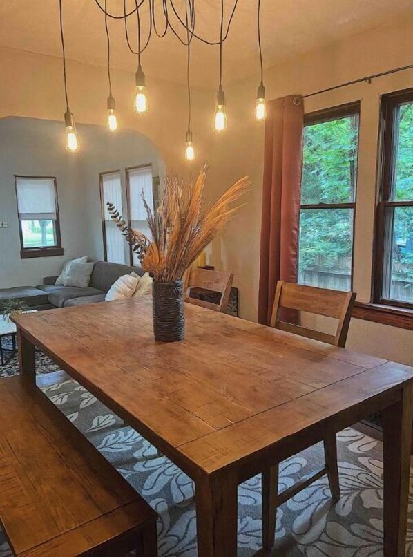 Enjoy meals in this dining area with a wooden table and benches, surrounded by a vase with dried plants and a hanging light fixture.