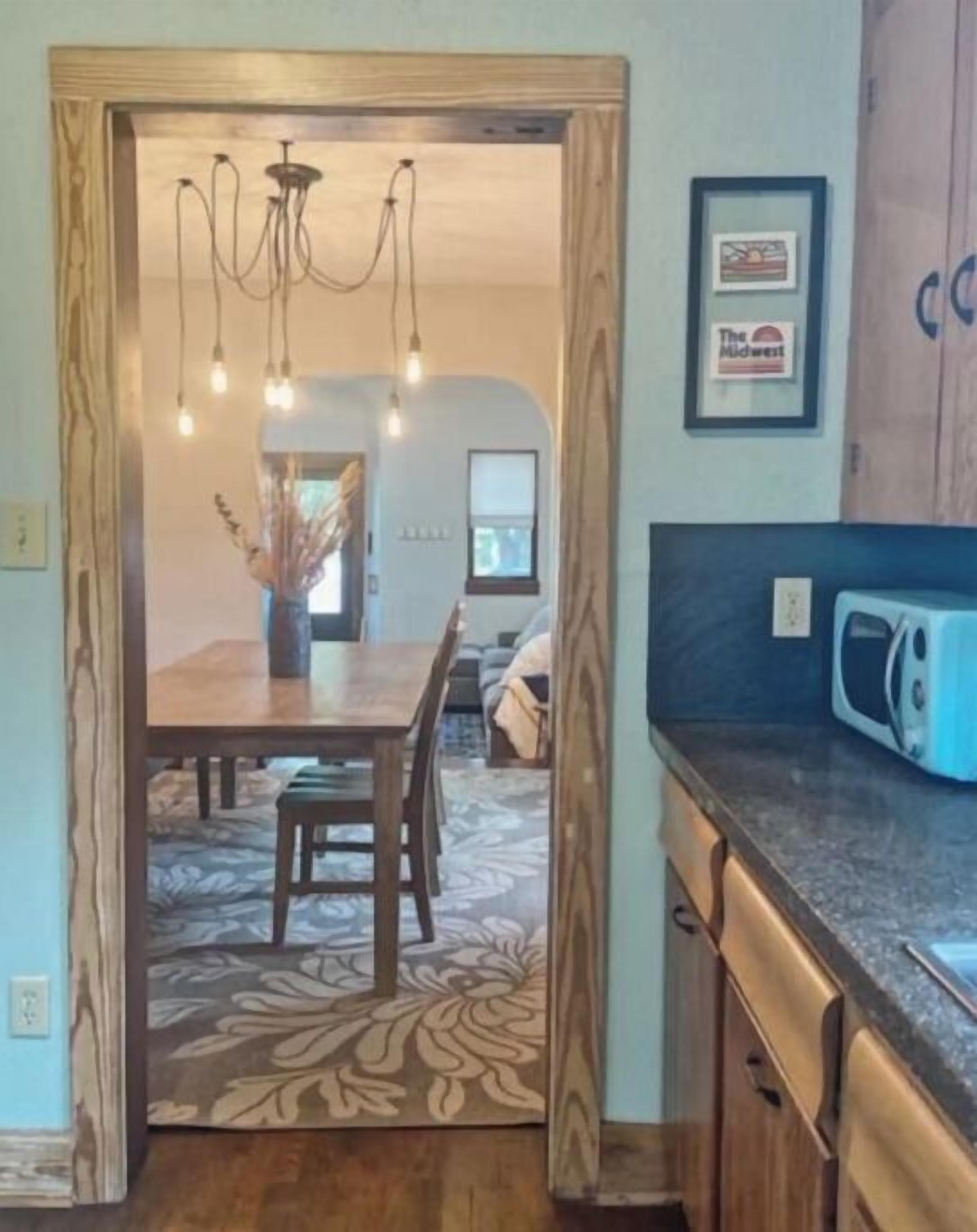 A kitchen with a wooden table, chairs, a chandelier, and a microwave.