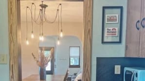 Une cuisine avec une table en bois, des chaises, un lustre et un four à micro-ondes.