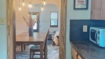 A kitchen with a wooden table, chairs, a chandelier, and a microwave.
