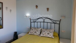 A bedroom with a bed, two pillows, a bedside table, a mirror, and decorative wall art.