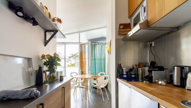 Et moderne køkken med træskabe, en stålbordplade og et spiseområde med hvide stole.