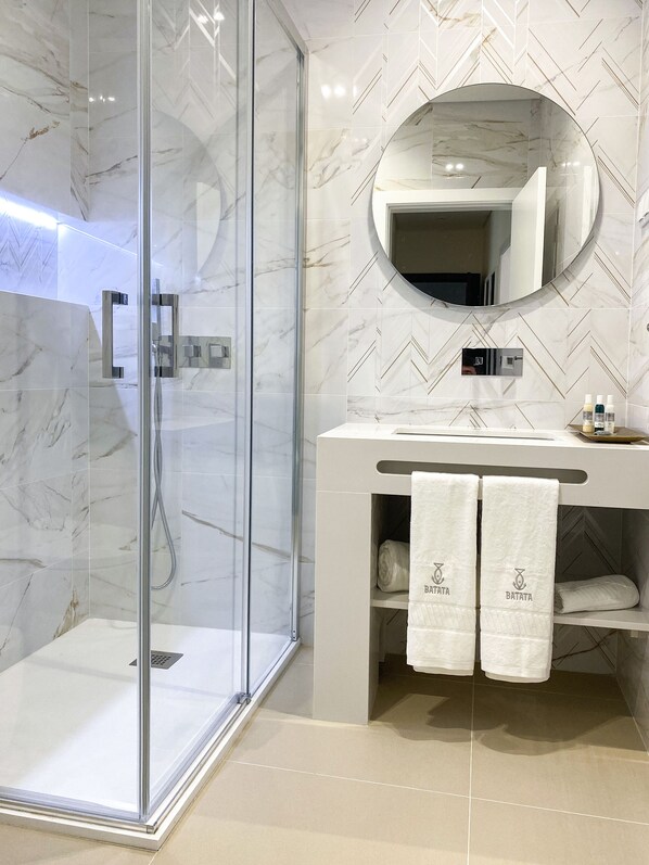 A modern bathroom with a glass-enclosed shower, a vanity with a mirror, and two towels hanging on the wall.