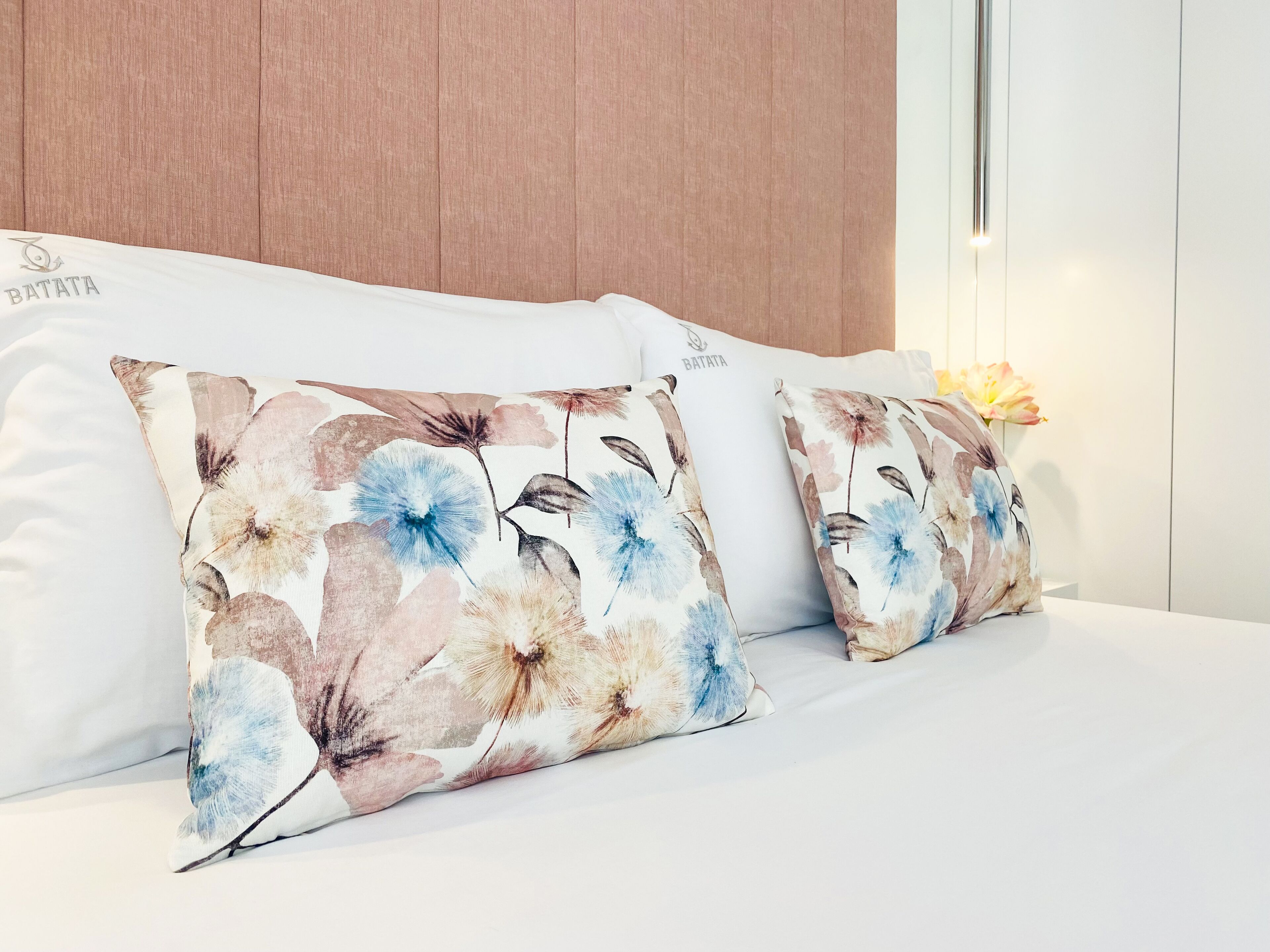 Ein Bett mit weißer Bettwäsche und zwei dekorativen Kissen mit Blumenmuster.