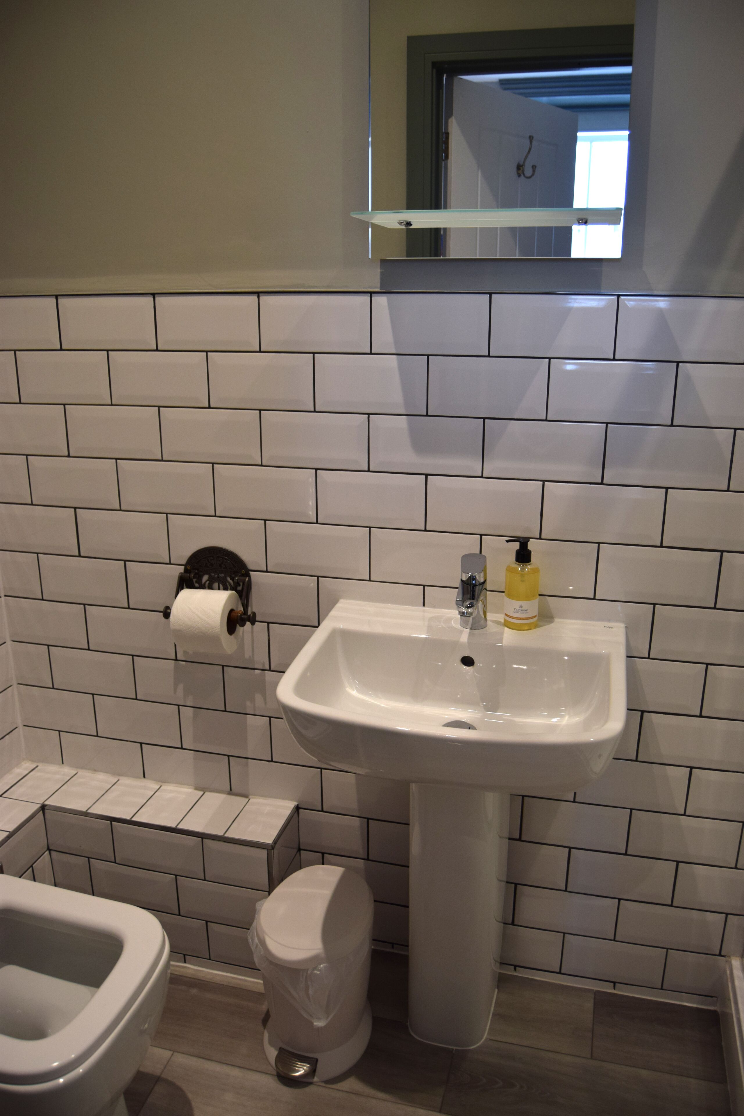 A bathroom with white subway tiles, a white sink, a toilet, and a roll of toilet paper on a holder.