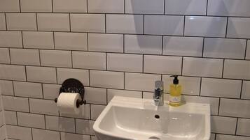 A bathroom with white subway tiles, a white sink, a toilet, and a roll of toilet paper on a holder.