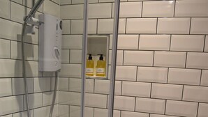 A shower with a handheld showerhead and a control panel, a glass door, and a tiled wall. - Crown Inn (Penzance)