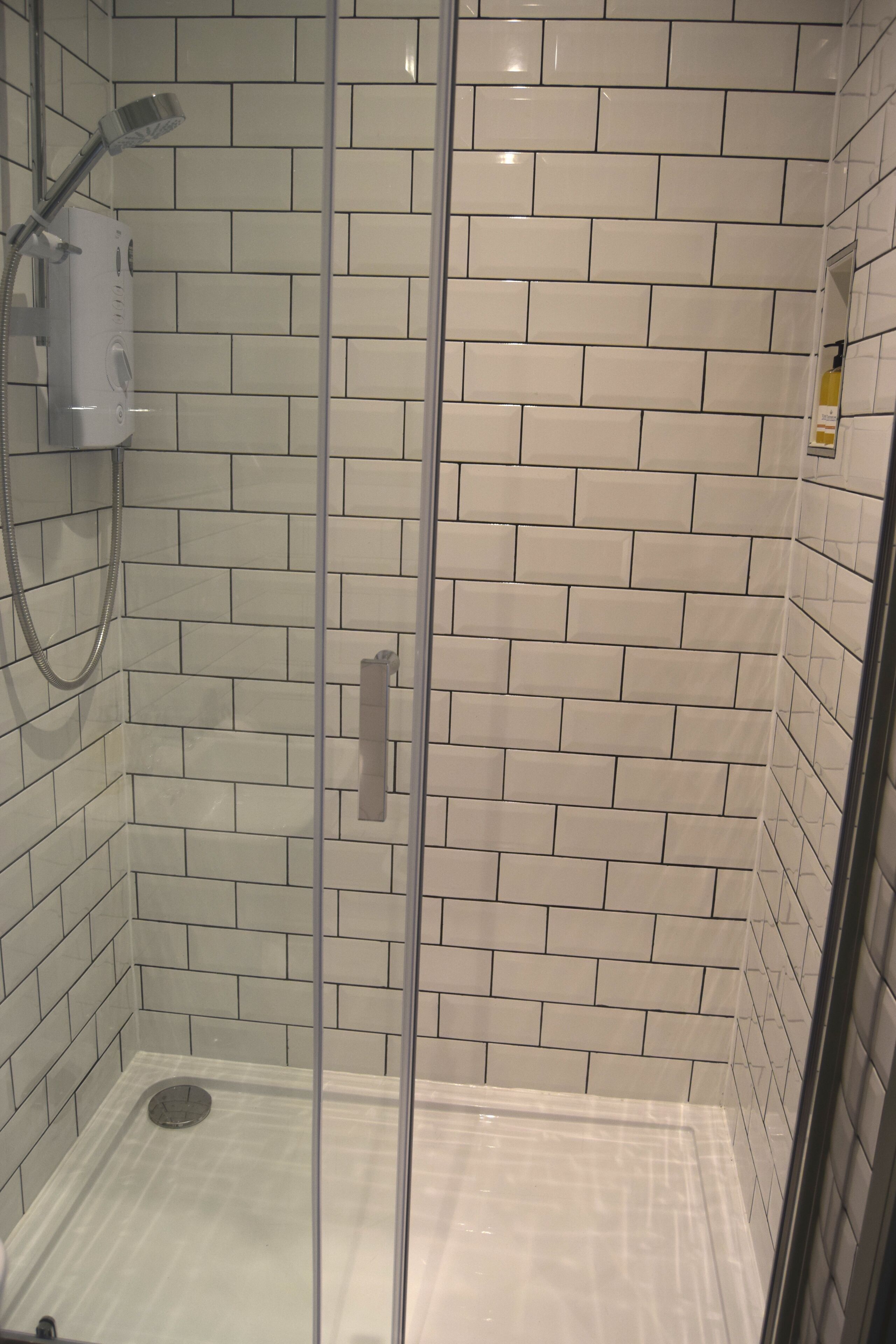 A glass-enclosed shower with white subway tiles on the walls and floor.