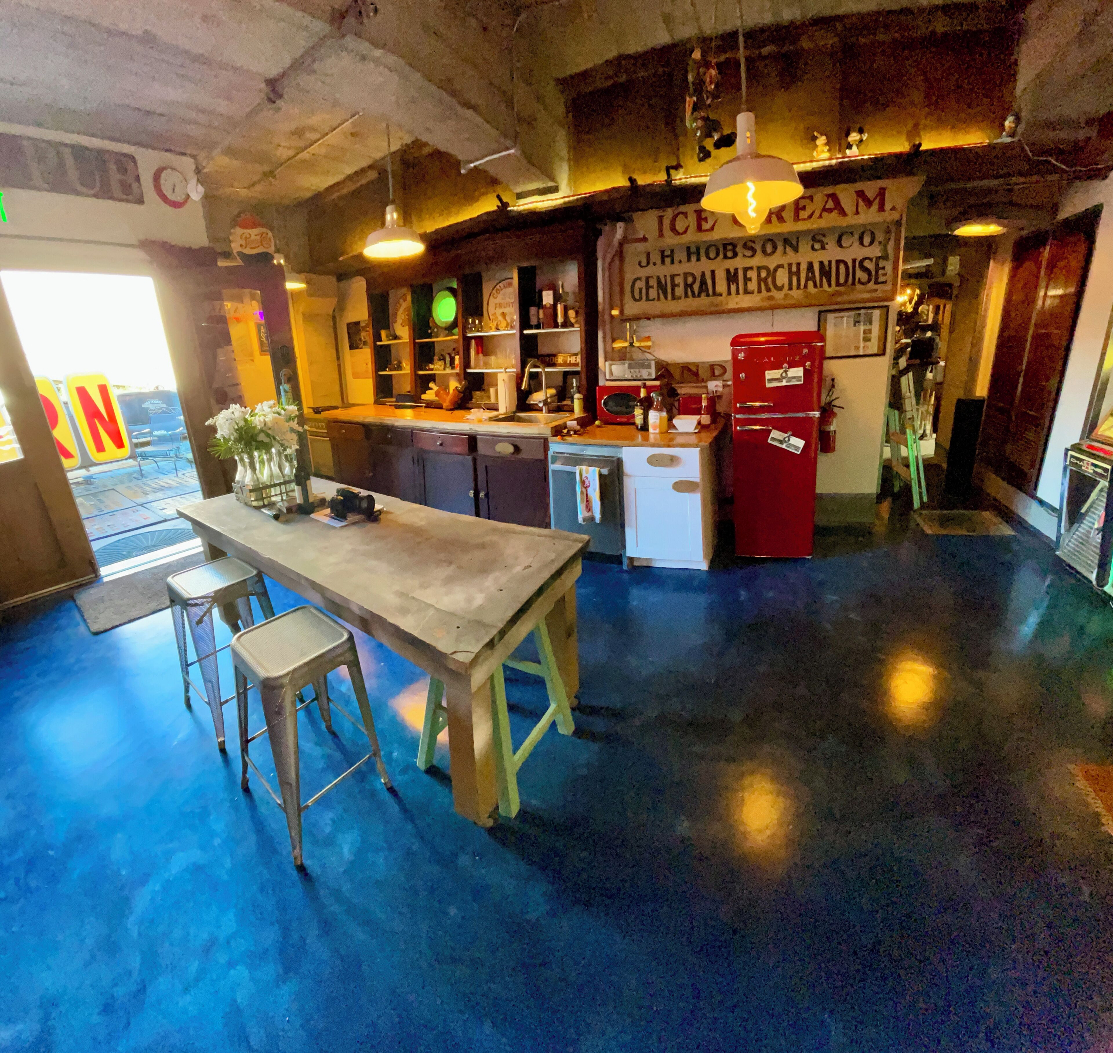 Un espace bar avec des tabourets, un comptoir et une enseigne indiquant « J.H. Hobson & Co., articles de quincaillerie et de marchandises générales ».