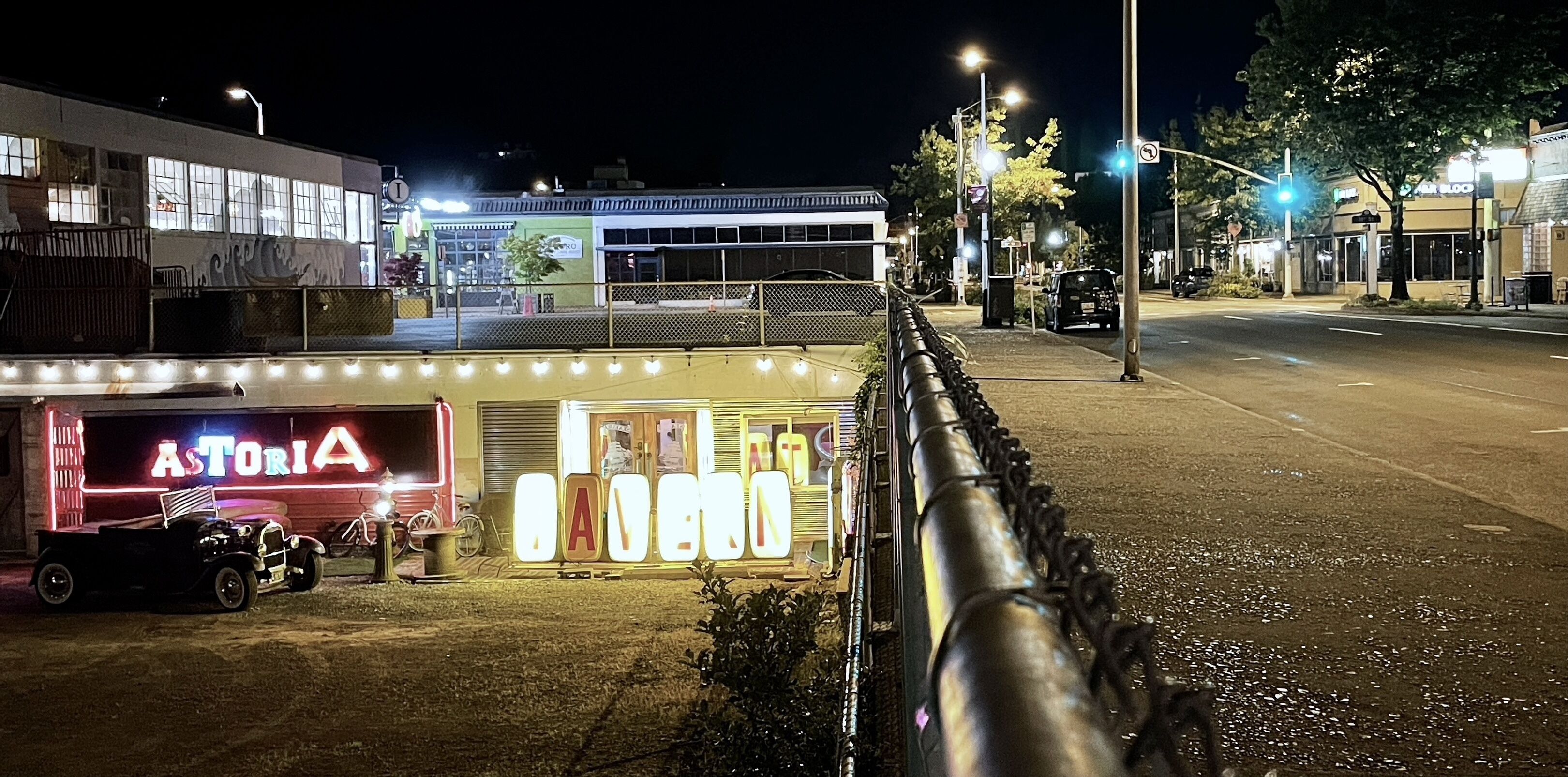 A street view at night with a neon sign for 'ASTORIA' and a vintage car parked in front.