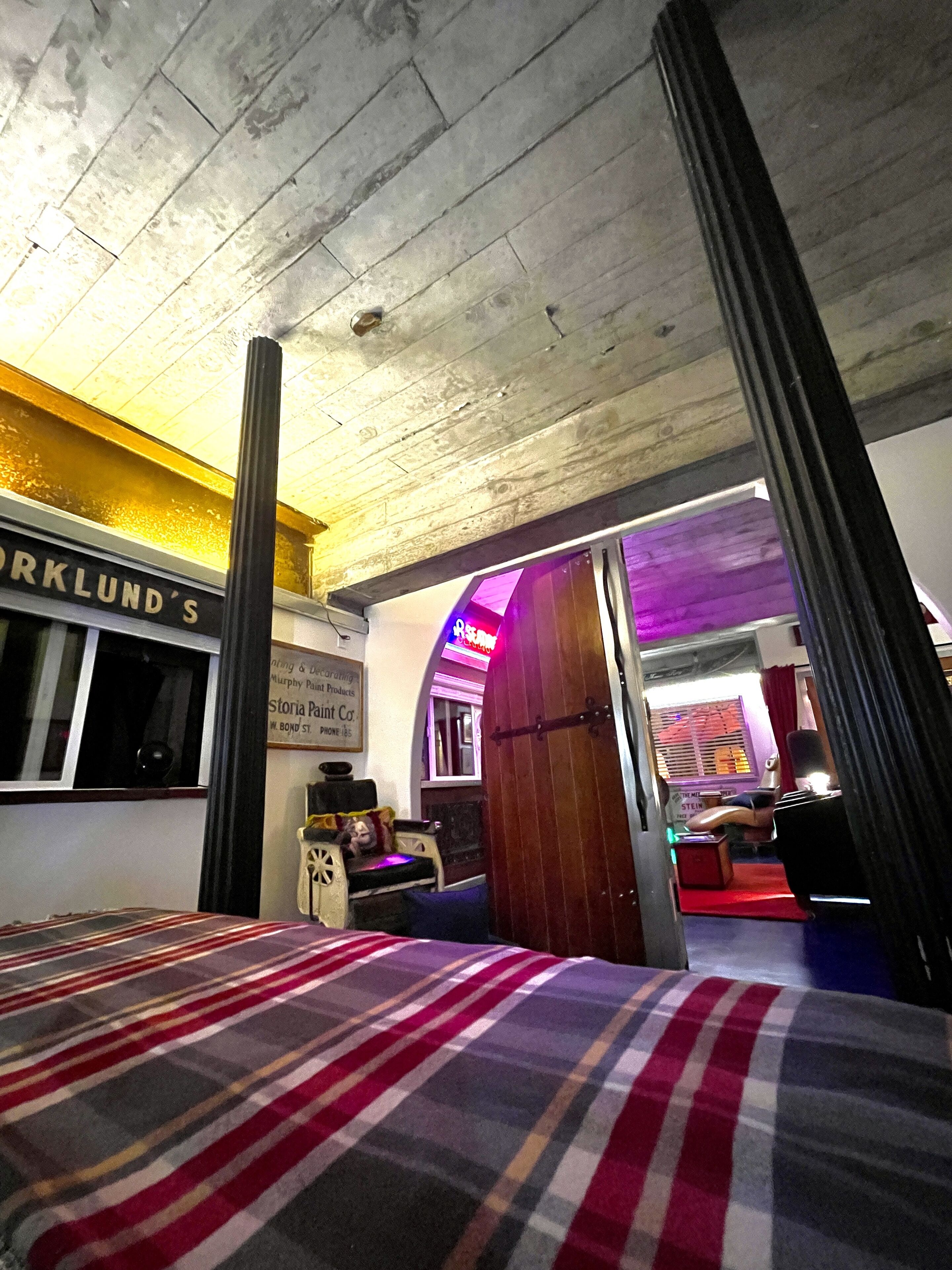 Una habitación con una cama, un ventanal, un cartel que dice 'Oaklund's' y una puerta que da a otra estancia.