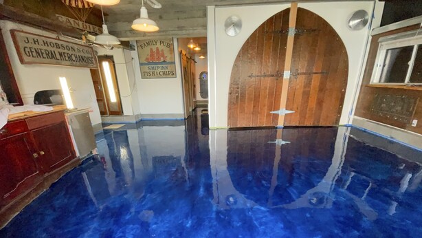 A room with a large, reflective blue floor, wooden cabinets, and a door with a ship's wheel design. - 1 of a kind (Astoria)