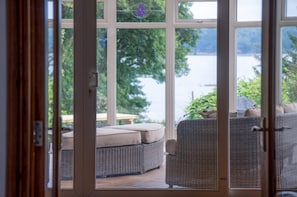 A view through a glass door to a patio area with wicker furniture and a view of a lake. - Sea View - 2 Bedroom Cottage - Wisemans Bridge - Saundersfoot (Saundersfoot)