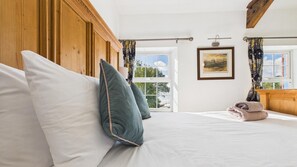 Een slaapkamer met een groot bed, een houten hoofdeinde, een ingelijst schilderij aan de muur en een raam met gordijnen.