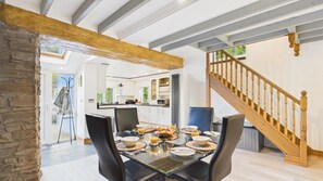 Een eetgedeelte met een gedekte tafel voor het ontbijt, een keuken op de achtergrond en een houten trap.