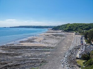 A coastal view with a rocky beach, a clear sky, and a forested area in the background.