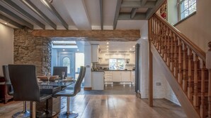A modern kitchen with white cabinets, a wooden staircase, and a dining area with a glass table and chairs. - Sea View - 2 Bedroom Cottage - Wisemans Bridge - Saundersfoot (Saundersfoot)