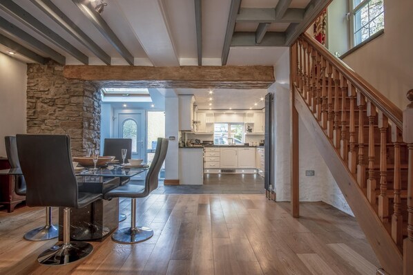 A modern kitchen with white cabinets, a wooden staircase, and a dining area with a glass table and chairs. - Sea View - 2 Bedroom Cottage - Wisemans Bridge - Saundersfoot (Saundersfoot)