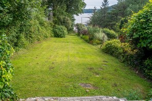 A well-maintained lawn with a stone pathway leading to a body of water, surrounded by dense greenery and trees.