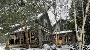 Een besneeuwde pad naar een rustiek stenen huis met een veranda en een verlicht interieur.