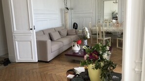Una sala de estar con un sofá color crema, una mesa de centro con un jarrón de flores y un comedor con una mesa de vidrio y sillas.
