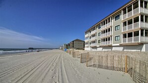Un hôtel situé en bord de mer, doté de nombreux balcons, d’une plage de sable et d’une jetée en arrière-plan.