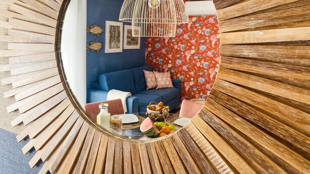 A circular mirror reflecting a living room with a blue sofa, floral wallpaper, and a hanging light fixture.