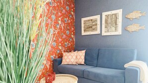 A room with a blue sofa, a round wicker table, a potted plant, and two framed pictures on the wall.