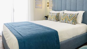 A neatly made bed with a blue and white bedspread, two patterned pillows, and a blue headboard.