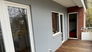 Una terraza cubierta de madera con un muro exterior gris y una sección de ladrillo rojo.