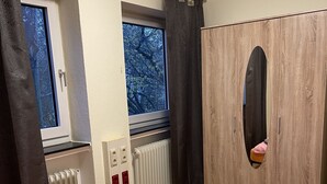 Un dormitorio con cama, armario, radiador y ventana con cortinas.