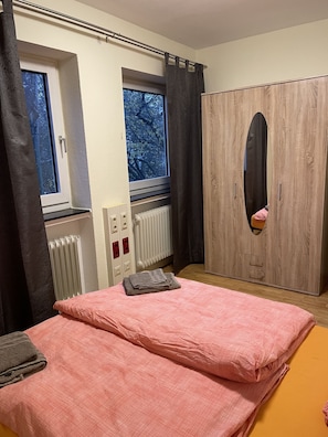 Ein Schlafzimmer mit Bett, Schrank, Heizkörper und einem Fenster mit Vorhängen.