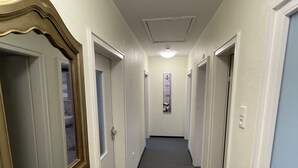 Un pasillo estrecho con paredes blancas y alfombra oscura. Hay puertas a ambos lados, y un cuadro enmarcado cuelga en la pared.