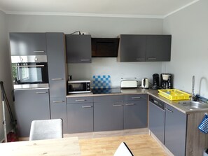 A modern kitchen with grey cabinets, a built-in oven, microwave, toaster, and coffee maker.