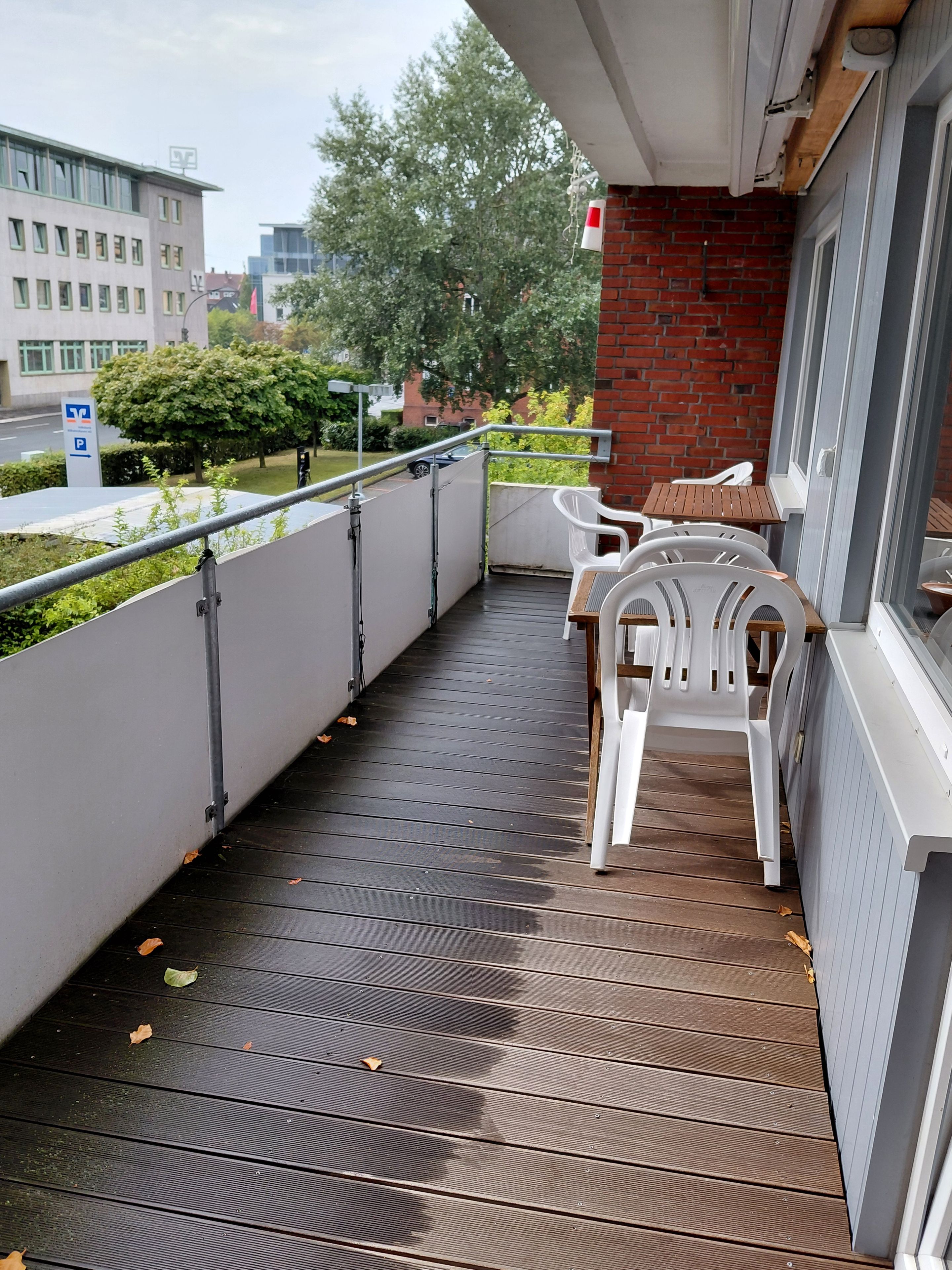 A balcony with a wooden floor, white plastic chairs, and a table.