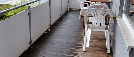 A balcony with a wooden floor, white plastic chairs, and a table.