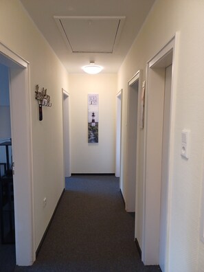 A narrow hallway with white walls and a carpeted floor, leading to doors on both sides.