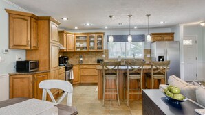 Una cocina con armarios de madera, microondas, refrigerador y comedor con mesa y sillas.
