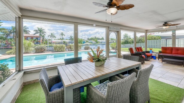 Un porche cubierto con vista a la piscina, mobiliario de mimbre, ventiladores de techo y un letrero que dice "BEACH HOUSE".